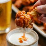 A close-up of a crispy buffalo cauliflower wing being dipped into a bowl of creamy ranch dressing.