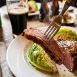 A close-up of a fork holding a piece of glazed corned beef and cabbage, with steam rising.
