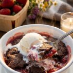 A close-up of a bowl of chocolate strawberry cobbler topped with melting vanilla ice cream.