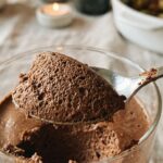 A macro close-up of a spoon lifting chocolate mousse, showing the tiny air bubbles and fluffy texture.