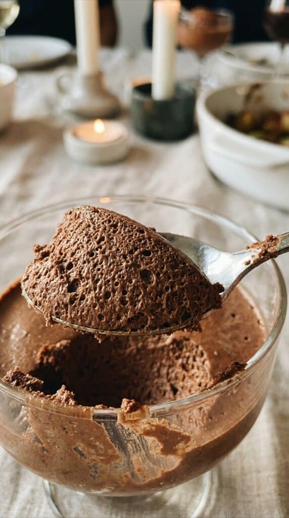 A macro close-up of a spoon lifting chocolate mousse, showing the tiny air bubbles and fluffy texture.