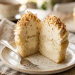 A close-up cross-section of a coconut cupcake cut in half, revealing a moist crumb and a creamy hidden filling inside.