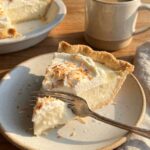 A close-up side view of a fork cutting into a slice of coconut cream pie, showing the layers.
