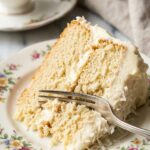 A close-up of a fork cutting into a moist slice of coconut cake on a floral plate.