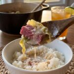 A close-up of a spoon lifting a piece of corned beef covered in creamy coconut sauce over rice.