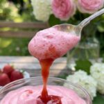 A close-up of a spoon lifting a fluffly dollop of pink strawberry cream.