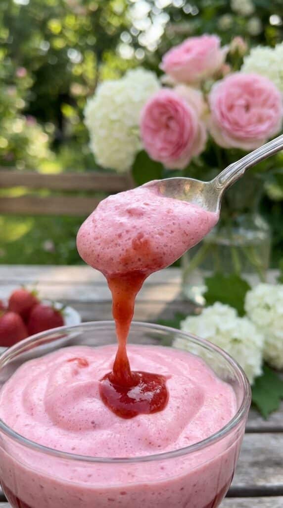 A close-up of a spoon lifting a fluffly dollop of pink strawberry cream.