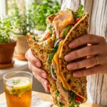 A close-up of hands holding a cottage cheese wrap sandwich with a bite taken out of it, showing its flexible texture.