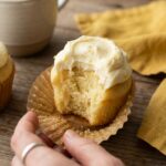 A close-up of a hand holding a lemon cupcake with a bite taken out, showing the fluffy texture inside.