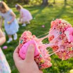 A close-up of a hand holding a pink cereal treat egg, pulling it apart to show the gooey marshmallow.