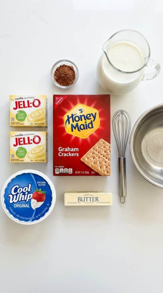 A flat lay showing boxes of graham crackers, vanilla pudding mix, cool whip, milk, and cocoa powder.