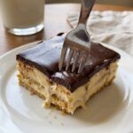 A close-up of a fork cutting into a soft slice of layered eclair cake on a plate.