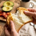 A close-up of hands tearing apart a piece of cloud bread, revealing its soft, airy interior texture.
