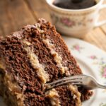 A close-up side view of a slice of German Chocolate Cake showing the filling layers between the chocolate sponge.