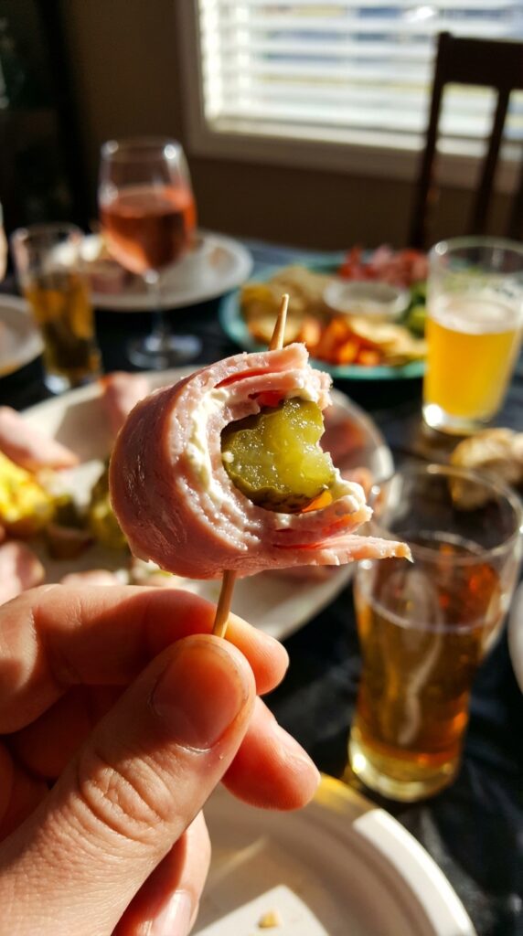 A close-up of a hand holding a single ham and pickle roll-up on a toothpick.