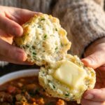 A close-up of a warm, herb-speckled biscuit split in half with butter melting into the center.