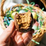 A close-up of a hand holding a chocolate peanut butter egg with a bite taken out, showing the texture.