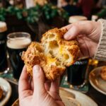 A close-up of hands pulling apart a cheese puff, revealing a hollow, steamy, cheesy center.