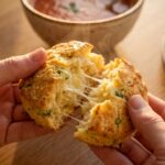 A close-up of hands pulling apart a warm cheesy biscuit, revealing a steaming fluffy interior.