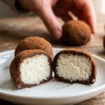 A close-up of an Irish potato candy cut in half, revealing a white coconut cream center surrounded by a brown cinnamon coating.