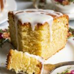 A close-up of a slice of moist lemon cake on a floral plate with a fork taking a bite.