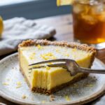 A close-up side view of a slice of lemon icebox pie showing the smooth yellow filling and whipped cream.