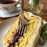A close-up of a fork taking a bite of lemon raspberry cake, showing a juicy berry pocket inside the crumb.