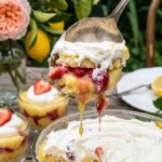 A close-up of a serving spoon lifting a scoop of layered lemon and strawberry trifle.