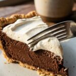 A close-up of a fork cutting into a slice of chocolate pie, showing the silky texture of the filling.
