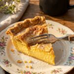 A close-up side view of a slice of chess pie showing the dense custard filling and crispy top layer.