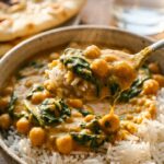 A close-up of a spoon lifting a bite of creamy chickpea curry and fluffy basmati rice from a bowl.