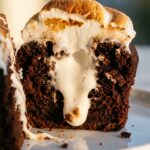 A close-up cross-section of a chocolate cupcake cut in half, showing a gooey marshmallow filling inside.
