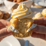A close-up of a hand peeling the wrapper off a mimosa cupcake, showing the fluffy cake texture.