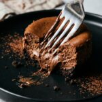 An extreme close-up of a fork cutting through a dense mini chocolate cheesecake showing the fudgy texture inside.