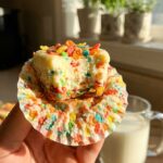 A close-up cross-section of a halved sweet potato cupcake, showing a moist orange interior and fluffy toasted marshmallow frosting.