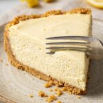 A close-up of a fork cutting into a creamy slice of lemon cheesecake, showing the smooth texture.