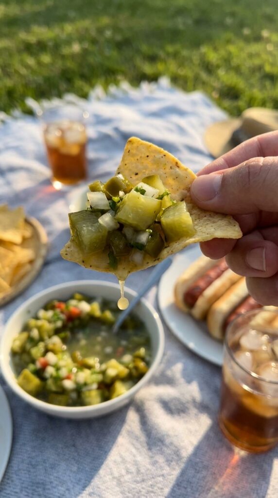 A close-up of a tortilla chip scooping up a large chunk of pickle salsa.