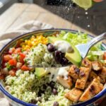 A close-up of a fork lifting a perfect bite of rice, beans, and avocado from a burrito bowl.