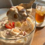 A close-up of a spoon lifting a scoop of creamy strawberry banana pudding, showing softened cookies and fruit.