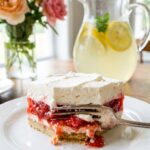 A close-up of a square slice of strawberry layered dessert on a plate with a fork.