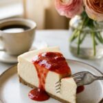 A close-up side view of a slice of strawberry cheesecake showing the creamy texture and crust layers.
