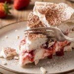 A close-up of a fork breaking through a slice of meringue cake, showing the crisp shell and soft cream.