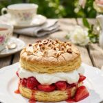 A close-up of a hazelnut shortcake topped with toasted meringue, filled with whipped cream and strawberries on a white plate.