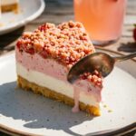 A close-up of a slice of strawberry ice cream cake showing the crust, vanilla layer, strawberry layer, and crunch topping.