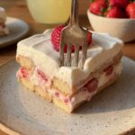 A close-up of a slice of strawberry icebox cake with a fork cutting through the soft, creamy layers.
