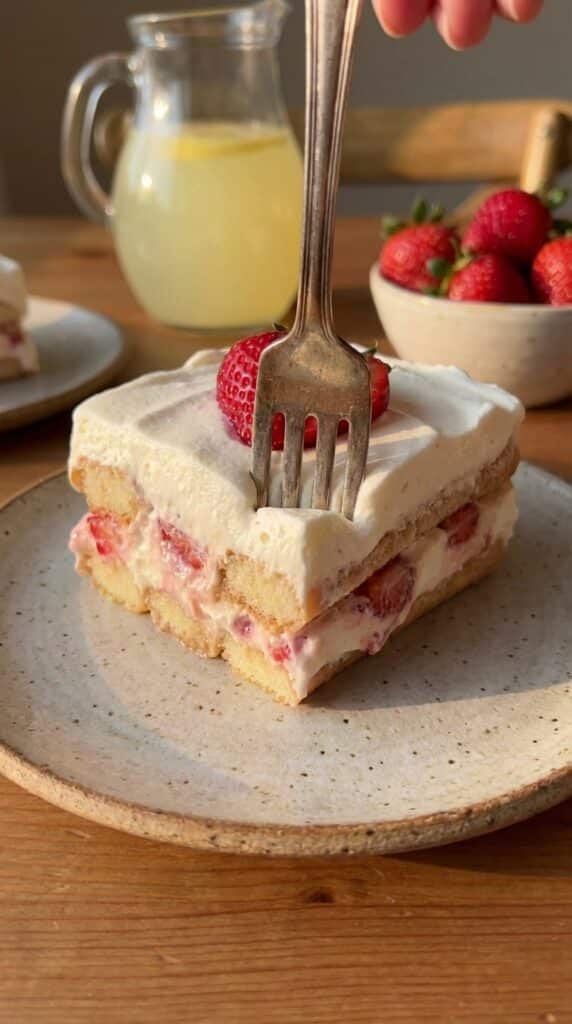 A close-up of a slice of strawberry icebox cake with a fork cutting through the soft, creamy layers.