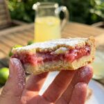 A close-up of a hand holding a bitten strawberry-lime bar, showing the gooey texture.