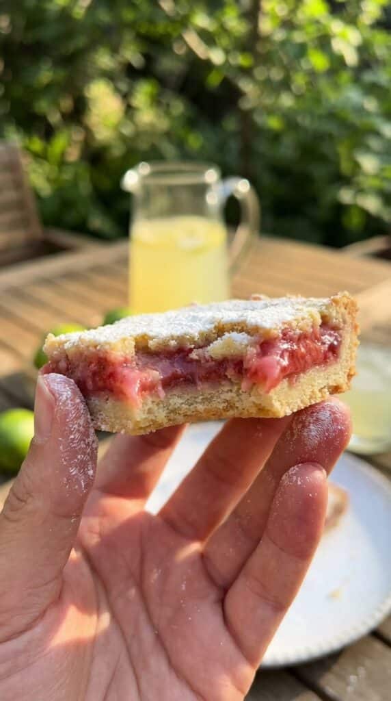 A close-up of a hand holding a bitten strawberry-lime bar, showing the gooey texture.