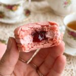 A close-up of a bitten pink macaron showing the jam center and chewy texture.