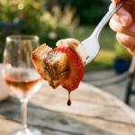 A close-up of a fork lifting a piece of strawberry, bread, and cheese with balsamic dressing dripping off.